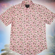 Load image into Gallery viewer, Full centered view of the "Magnolia PI" 7-Strong Adult button down shirt, featuring white and green magnolia flowers patterned all over a light pink background. The shirt itself is displayed against a palm tree tropical background.