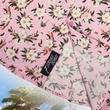 Load image into Gallery viewer, Bottom sweep tag close up view of the "Magnolia PI" 7-Strong Adult button down shirt, featuring white and green magnolia flowers patterned all over a light pink background. The shirt itself is displayed against a palm tree tropical background.