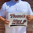 Load image into Gallery viewer, A midsection view of a male model wearing the 7-Strong "Stay" button down, a white shirt with staggered, hollowed out semicolons outlined in teal and purple - the colors for suicide awareness. Model is holding a handwritten sign saying "There's Help."