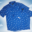 Load image into Gallery viewer, A complete view of the adult and youth 7-Strong "Paper Planes" button down shirts overlapping one another - featuring various sizes and designs of paper airplanes, some with dotted trails behind them against a royal blue background. The shirt is displayed against a faced background of the shirt details.