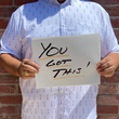Load image into Gallery viewer, A midsection view of a male model wearing the 7-Strong "Stay" button down, a white shirt with staggered, hollowed out semicolons outlined in teal and purple - the colors for suicide awareness. Model is holding a handwritten sign saying "You Got This!"