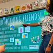 Load image into Gallery viewer, Female model wearing the 7-Strong Class Act button down while teaching a class and pointing towards an electronic blackboard.