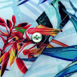 Load image into Gallery viewer, Midsection button close up view of the 7-Strong "Tropic of Conversation" adult button down shirt - featuring several different floral plants in large, vibrant print against a faded background of other plants and florals. The shirt is featured against a lush, green rainforest background.