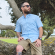 Load image into Gallery viewer, Medium shot of a male model, sitting on a log, looking off in to the distance wearing the baby blue 7-Strong EveryWEAR short sleeve button down. Design is baby blue with subtle white 7-bolts featured all over, side-by-side in white.