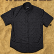 Load image into Gallery viewer, Full, centered view of the 7-Strong Bandido shirt, a black and gray paisley shirt design with black pearl snap buttons. Shirt is featured against a sepia toned parchment paper resembling a "wanted" sign.