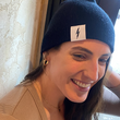 Load image into Gallery viewer, Female model smiling and looking away while wearing the black 7-Bolt beanie, reaching up to playfully adjust it.