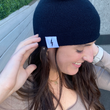 Load image into Gallery viewer, Female model smiling and looking away while wearing the black 7-Bolt beanie, reaching up to playfully adjust it.