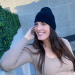 Load image into Gallery viewer, Female model smiling and looking up while wearing the black 7-Bolt beanie, reaching up to playfully adjust it.