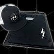 Load image into Gallery viewer, Folded and centered close up of the 7-Strong black Branded tee, featuring a 7-bolt logo left justifed in white. It is paired with the black "Branded" trucker hat with raised x-badge patch. Shirt is featured against a black geometric background.
