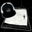Load image into Gallery viewer, Folded and centered close up of the 7-Strong white Branded tee, featuring a 7-bolt logo left justifed in white. It is paired with the black "Branded" trucker hat with raised x-badge patch. Shirt is featured against a black geometric background.