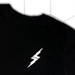 Load image into Gallery viewer, Front top of shoulder, left lapel look of the 7-Strong black Branded tee, featuring a 7-bolt left justified in white. Shirt is featured against a white geometric background.
