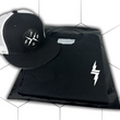 Load image into Gallery viewer, Folded and centered close up of the 7-Strong black Branded tee, featuring a 7-bolt logo left justifed in white. It is paired with the black "Branded" trucker hat with raised x-badge patch. Shirt is featured against a white geometric background.