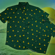 Load image into Gallery viewer, A centered, overlapping view of the 7-Strong "Duck O' The Irish" adult and youth button down, featuring a deep green water-replicating background with various rubber ducks swimming along the waves. The shirt is featured against a green river scenic with a giant inflatable duck in the background.