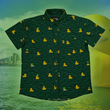 Load image into Gallery viewer, A centered view of the 7-Strong "Duck O' The Irish" youth button down, featuring a deep green water-replicating background with various rubber ducks swimming along the waves. The shirt is featured against a green river scenic with a giant inflatable duck in the background.
