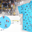Load image into Gallery viewer, A 3/4 full view of the youth 8-Bit Hat Trick button down - featuring various 8-bit inspired scenes from hockey games on a light blue ice-like background. The shirt is featured against a ice hockey floor with hats strewn about. The bottom left features a detail circle with a close up of a few scenes from the shirt.