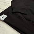 Load image into Gallery viewer, Bottom cuff angled view of the 7-Strong Midnight Long Sleeve Hoodie, a black hoodie with black shadow font of the 7-Strong Brand logo. The hoodie is show against a white brick backdrop.