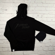 Load image into Gallery viewer, Full view of the 7-Strong Midnight Long Sleeve Hoodie, a black hoodie with black shadow font of the 7-Strong Brand logo. Alongside the black 7-Bolt Beanie with a white 7-Bolt tag on the cuff. The hoodie is show against a white brick backdrop.