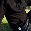 Load image into Gallery viewer, Midsection view of a model wearing the 7-Strong Midnight long sleeve Hoodie, sitting on the grass and posing.