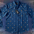 Load image into Gallery viewer, Full layout of "Call Me Old Fashioned" adult long sleeve button-down. Features elements of an Old Fashioned cocktail (bottle of bourbon, glasses, oranges, stirrers, and ice) against a blue background which faintly spells out an Old Fashioned recipe. Shirt is on a background featuring a finished Old Fashioned. The shirt is displayed on the background of a bartender making an old fashioned cocktail.