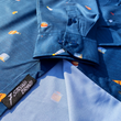 Load image into Gallery viewer, Sweep tag and sleeve view of "Call Me Old Fashioned" adult long sleeve button-down. Features elements of an Old Fashioned cocktail (bottle of bourbon, glasses, oranges, stirrers, and ice) against a blue background which faintly spells out an Old Fashioned recipe.