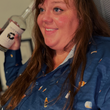 Load image into Gallery viewer, Female model smiling and holding a bottle of whiskey wearing the "Call Me Old Fashioned" adult long sleeve button-down. Features elements of an Old Fashioned cocktail (bottle of bourbon, glasses, oranges, stirrers, and ice) against a blue background which faintly spells out an Old Fashioned recipe.
