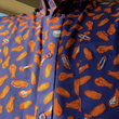 Load image into Gallery viewer, Medium close up of male model wearing 7-Strong's Wingman button down, featuring various flats and drumstick chicken wings and dip sauces against a deep blue background.