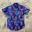 Load image into Gallery viewer, Full centered view of the 7-Strong "Neon Coast" adult button down shirt. Featuring vibrant teal, pink, and blue palm fronds, overlapping throughout the shirt, against a black/deep purple background. The shirt is laid out on the sand of a beach.
