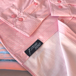 Load image into Gallery viewer, Bottom sweep view of the pink long sleeve EveryWEAR adult button up. Pattern is subtle white 7-Bolts lined up all against each other across a pink background. The shirt is featured on a soft background of a wave hitting the beach.