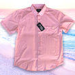 Load image into Gallery viewer, Full centered view of the pink short sleeve EveryWEAR adult button up. Pattern is subtle white 7-Bolts lined up all against each other across a pink background. The shirt is featured on a soft background of a wave hitting the beach.