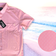 Load image into Gallery viewer, 3/4 full view of the pink short sleeve EveryWEAR adult button up. Pattern is subtle white 7-Bolts lined up all against each other across a pink background. The shirt is featured on a soft background of a wave hitting the beach. Bottom right corner features a detail circle of the bolts up close.