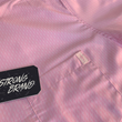 Load image into Gallery viewer, Corner pocket view of the pink short sleeve EveryWEAR adult button up. Pattern is subtle white 7-Bolts lined up all against each other across a pink background. The shirt is featured on a soft background of a wave hitting the beach.