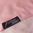 Load image into Gallery viewer, Bottom sweep tag view of the pink short sleeve EveryWEAR adult button up. Pattern is subtle white 7-Bolts lined up all against each other across a pink background. The shirt is featured on a soft background of a wave hitting the beach.