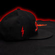 Load image into Gallery viewer, Full centered side look at the Black 7-Strong Sideline Script hat, with red embroidered 7-Bolt on the side. Hat is laid on the 7-Strong Sideline Script shirt and a red and black fusion background.