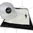 Load image into Gallery viewer, Folded and centered close up of the 7-Strong white Branded tee, featuring a 7-bolt logo left justified in white. It is paired with the white "Branded" performance hat with raised x-badge patch. Shirt is featured against a white geometric background.