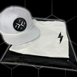 Load image into Gallery viewer, Folded and centered close up of the 7-Strong white Branded tee, featuring a 7-bolt logo left justified in black. It is paired with the white "Branded" performance hat with raised x-badge patch. Shirt is featured against a black geometric background.