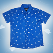 Load image into Gallery viewer, A full view of the youth 7-Strong "Paper Planes" button down shirt - featuring various sizes and designs of paper airplanes, some with dotted trails behind them against a royal blue background. The shirt is displayed against a faced background of the shirt details.