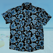 Load image into Gallery viewer, Full view of the 7-Strong youth Electric Palms shirt, a collection of electric blue palm fronds featured against a black shirt. Shirt is displayed against a scenic beach background.
