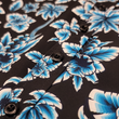 Load image into Gallery viewer, Midsection button view of the 7-Strong youth Electric Palms shirt, a collection of electric blue palm fronds featured against a black shirt. Shirt is displayed against a scenic beach background.