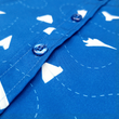 Load image into Gallery viewer, A mid-button view of the youth 7-Strong "Paper Planes" button down shirt - featuring various sizes and designs of paper airplanes, some with dotted trails behind them against a royal blue background. The shirt is displayed against a faced background of the shirt details.