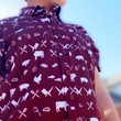 Load image into Gallery viewer, A middle close up, free standing view of a youth male model wearing the 7-Strong youth "Smoke Show" button up, a deep maroon red colored shirt with rows of various barbecue and cookout related items and delicacies silhouetted in white.