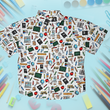 Load image into Gallery viewer, Full centered view of 7-Strong Class act button-down featuring various classroom items such as pencils, rulers, globes, notebooks, apples, protractors, etc against a white graph paper background. Shirt is against a background of school supplies.