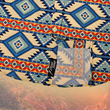 Load image into Gallery viewer, The bottom sweep portion of a short-sleeve button-down shirt featuring a bold Aztec-inspired pattern in shades of blue, orange, and cream. The intricate geometric design gives off a strong Southwest vibe. The shirt is set against a desert landscape background with towering red rock formations and a warm sunset sky, enhancing its rugged, adventurous aesthetic."