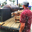Load image into Gallery viewer, A male model, from the back, looking at a BBQ smoker wearing the 7-Strong adult "Smoke Show" button up, a deep maroon red colored shirt with rows of various barbecue and cookout related items and delicacies silhouetted in white.