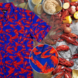 Load image into Gallery viewer, Full view of the adult 7-Strong Dat Boil shirt, with design circle in center, showing off details of deep navy blue with red crawfish patterned throughout overlapping one another. The shirt itself sits on a background image of items from a Crawfish Boil such as crawfish, seasoning, corn, and potatoes.