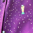 Load image into Gallery viewer, Middle button close up view of the Cup of Life adult button up, a off-maroon colored shirt decorated throughout with falling gold confetti and depictions of the World Cup statue. The shirt is laid out on a grass pitch.