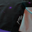 Load image into Gallery viewer, Bottom sweep tag view of the 7-Strong "Flux Capacity" short sleeve button down, showcasing bursts and lines of purple light peering through a black grid of cubes. The background is of a fashion show runway in purple hue.