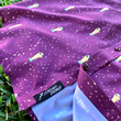 Load image into Gallery viewer, Bottom sweep tag portion view of the Cup of Life adult button up, a off-maroon colored shirt decorated throughout with falling gold confetti and depictions of the World Cup statue. The shirt is laid out on a grass pitch.