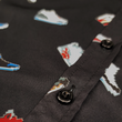 Load image into Gallery viewer, Midsection close up view of the adult short sleeve version of "Got 'Em!" The button down features various athletic fashion sneakers in an 8-bit format arranged all over a black shirt. The shirt is featured against a background of a basketball player on the court, noticeable sneakers being worn