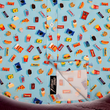 Load image into Gallery viewer, Bottom sweep tag section view of the 7-Strong "Cheat Day" adult button down featuring various snacks, treats, and fast food features on a light blue shirt. The shirt is displayed against a background of a gym weight rack.