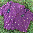 Load image into Gallery viewer, Full view of the Cup of Life adult and youth button ups, overlapping one another, a off-maroon colored shirt decorated throughout with falling gold confetti and depictions of the World Cup statue. The shirt is laid out on a grass pitch.